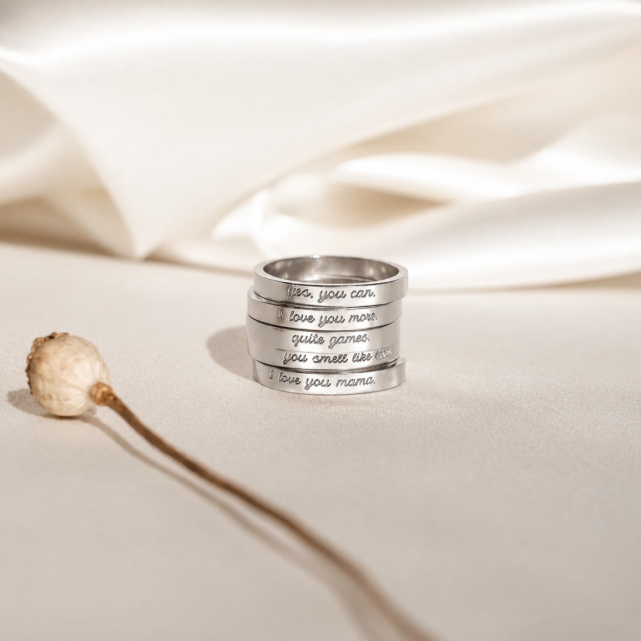 Stack of silver rings with engraved text on a beige fabric background